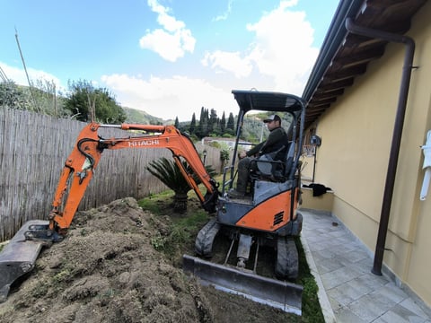Orange Hitachi mini excavator with operator in cab on residential construction site beside yellow building