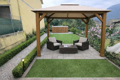 Wooden pergola with seating area in residential backyard featuring patio furniture, manicured lawn, and mountain views