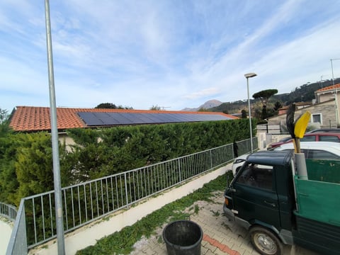 Rooftop with solar panels on house overlooking residential area with metal railing, parked vehicles, and blue sky